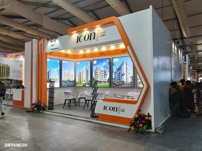 Modern exhibition stall decoration by ICON estd 1980 featuring bold orange and white branding, illuminated graphics, premium product displays, and a welcoming meeting space at a trade show.