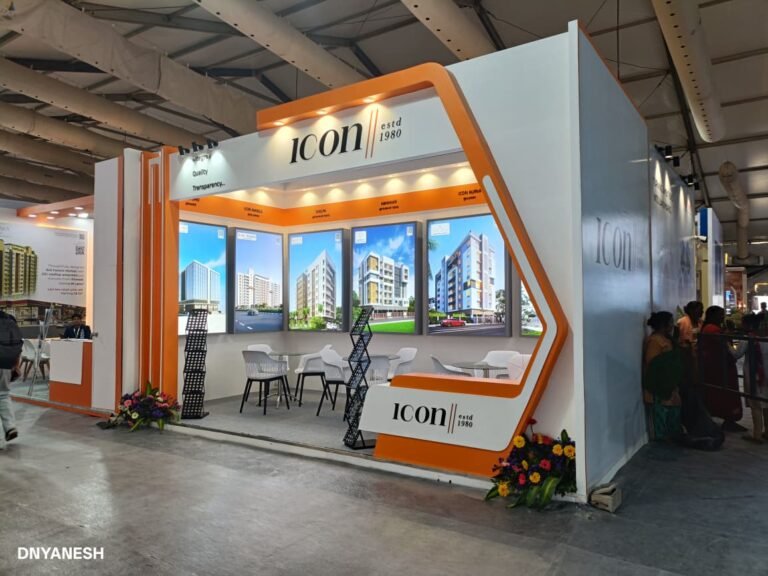 Modern exhibition stall decoration by ICON estd 1980 featuring bold orange and white branding, illuminated graphics, premium product displays, and a welcoming meeting space at a trade show.