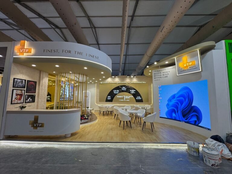 VTP Realty exhibition stall featuring elegant curved architecture, premium branding, LED display screens, modern seating, and luxury exhibition booth decoration at a real estate trade show.