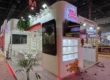 3D exhibition stall design for Jabsons Foods featuring illuminated branding, LED display screens, modern product display shelves, and an open meeting area by a premier exhibition stall design company.